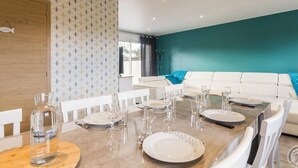 Un espace de salle à manger moderne avec une table en bois dressée pour quatre personnes, des chaises blanches et un mur d’accent de couleur turquoise.