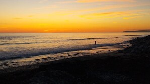 Une plage au coucher du soleil, avec une eau calme et une côte rocheuse.