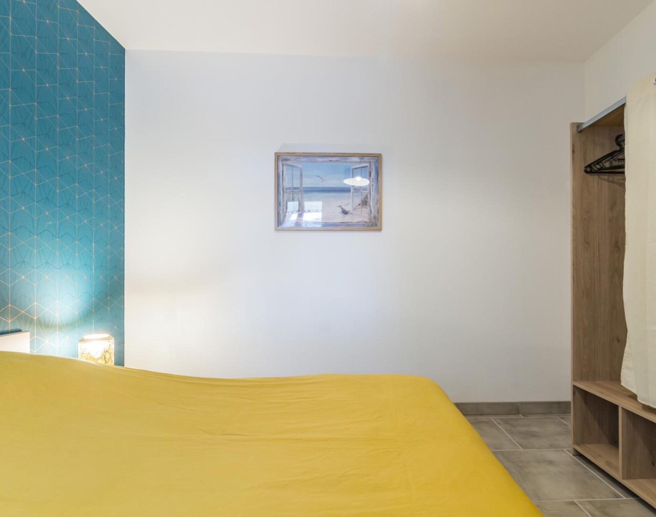 Una habitación con cama, ventana con vistas, armario de madera y pared azul con estampado.