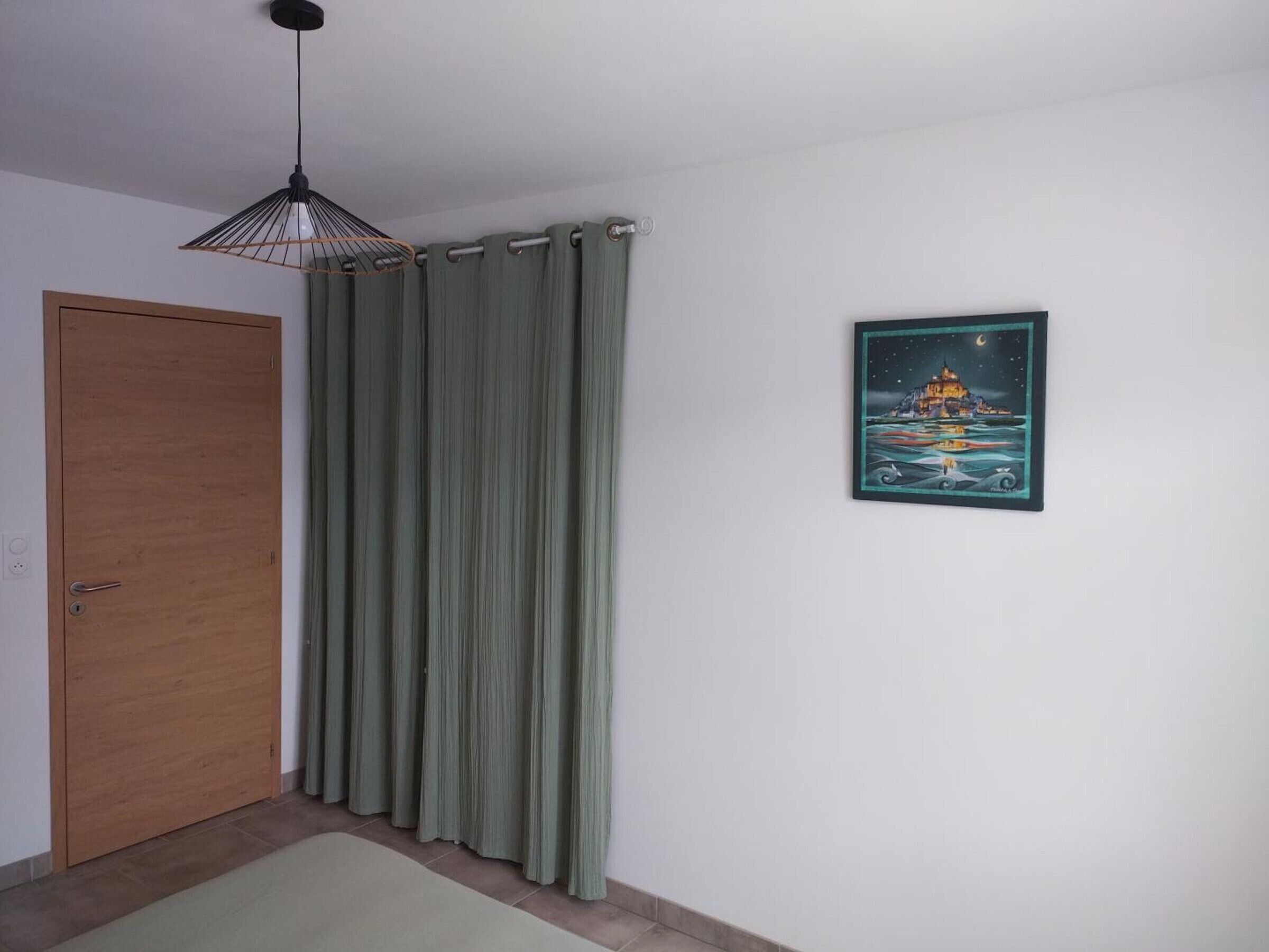 A room with a wooden door, green curtains, a hanging light fixture, and a framed picture on the wall.