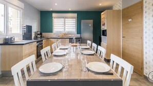 Une cuisine moderne avec un coin repas, comprenant une longue table dressée pour six personnes, un réfrigérateur et un four à micro-ondes.