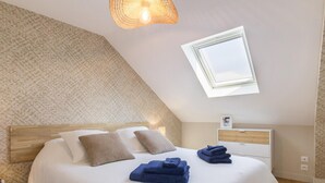 Un dormitorio con techo inclinado, tragaluz, cama con ropa de cama blanca y cabecera de madera.