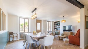 Amplia sala de estar con un piso de madera en espiga, una zona de comedor con una mesa larga y sillas, un televisor y una estantería.