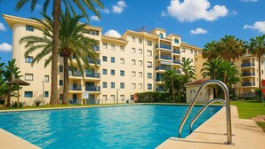 A swimming pool with a metal ladder, surrounded by palm trees and a multi-story building with balconies. - Charming Beachfront Apartment in Estepona with Wi-Fi (Estepona)