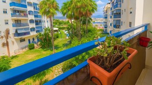 A balcony with a potted plant, overlooking a residential area with multiple buildings and a clear view of the sea. - Charming Beachfront Apartment in Estepona with Wi-Fi (Estepona)
