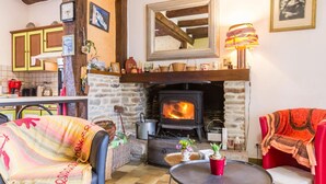 Una sala de estar acogedora con chimenea de piedra, un comedor con armarios amarillos y un sillón rojo con un cojín estampado.