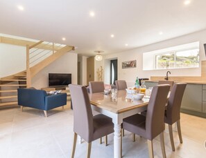 A modern living room with a dining area, a TV, and a staircase.