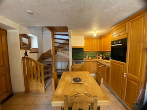 A kitchen with wooden cabinets, a wooden table, and a staircase leading to another level.