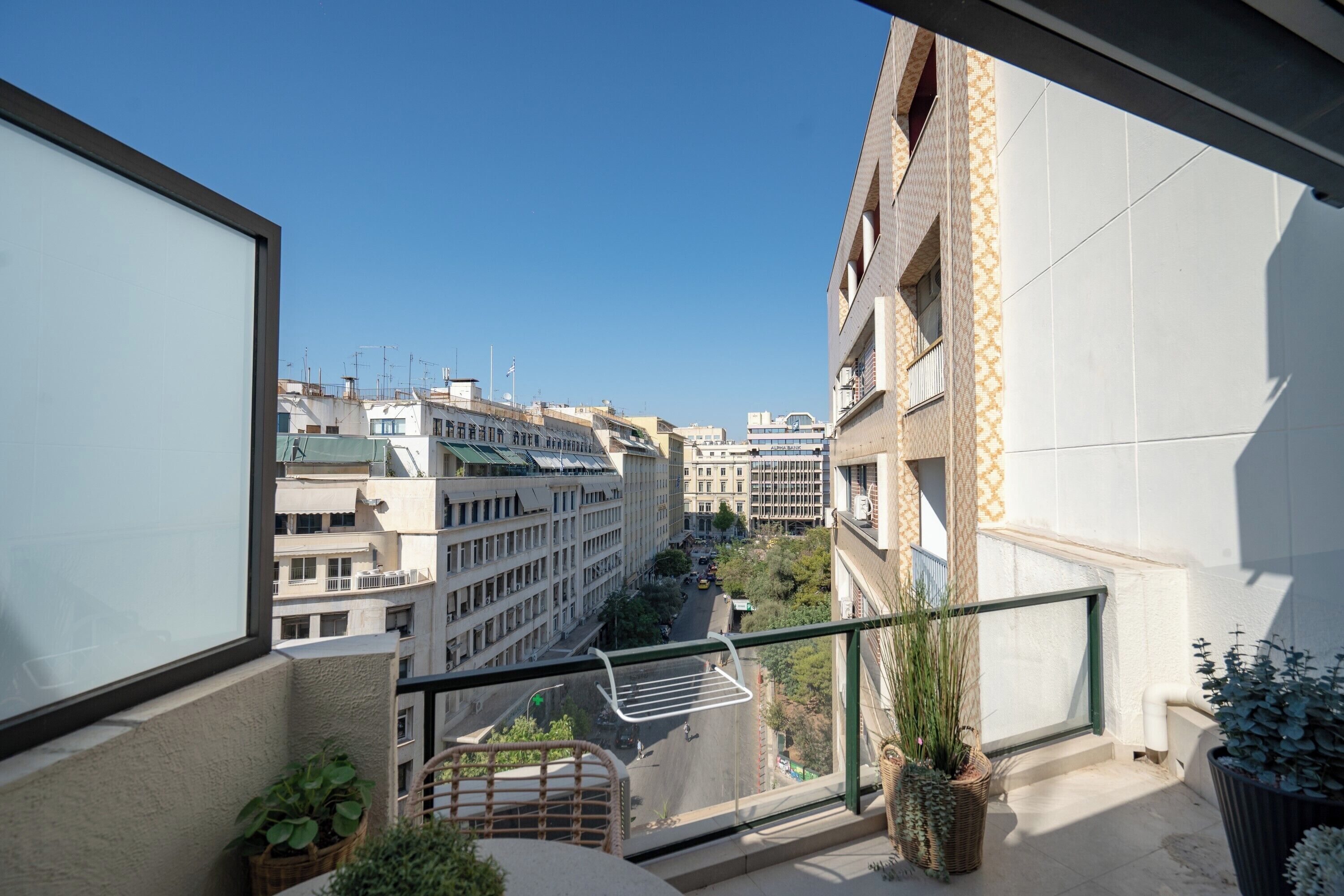 A balcony with a view of city buildings, a wicker chair, and potted plants.