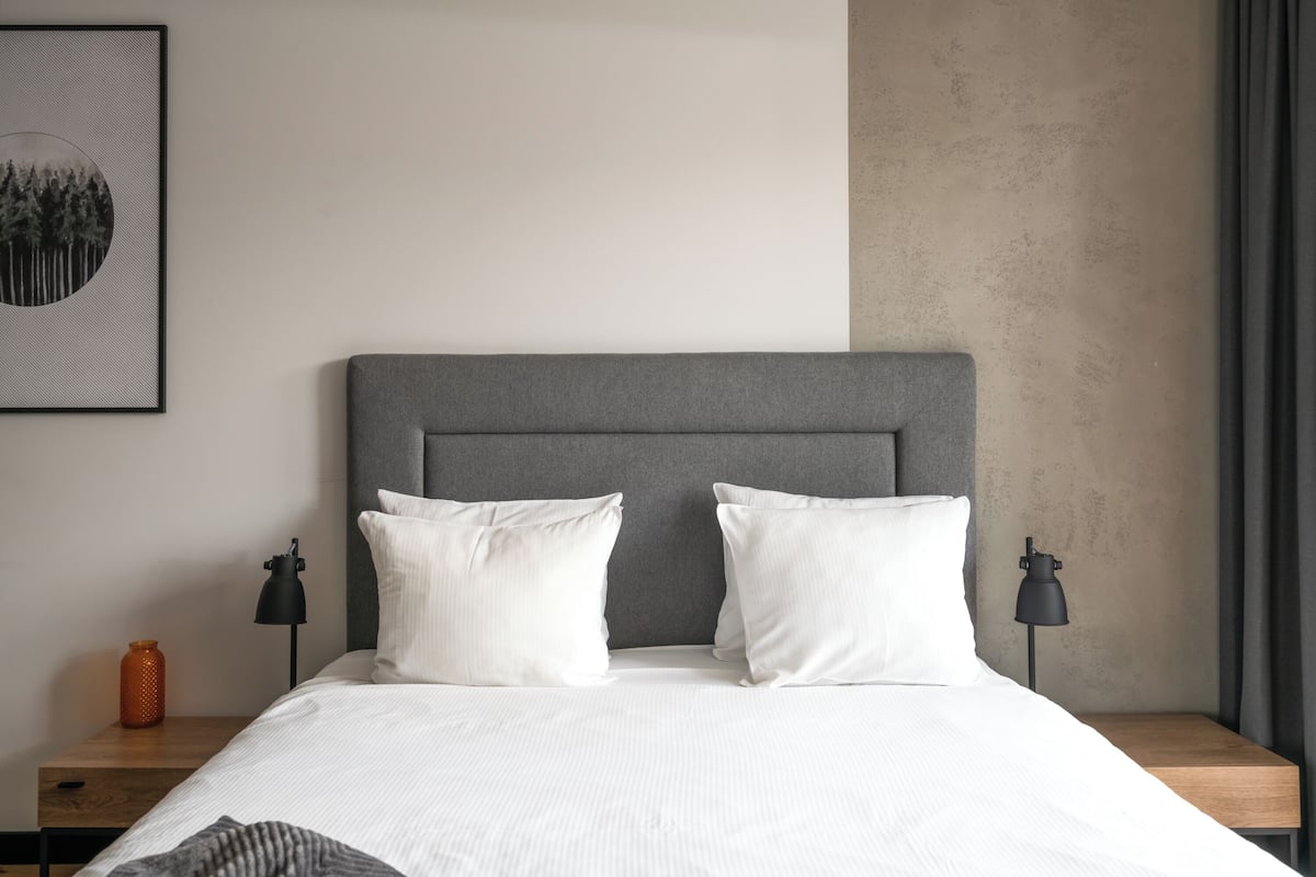 A neatly made bed with a grey headboard, two bedside lamps, and a framed picture on the wall.