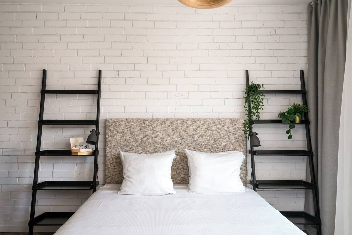 A bed with white bedding, two pillows, a headboard with a textured pattern, and two black metal shelves on either side.