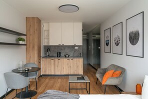 A modern hotel room with a kitchenette, a dining area, a seating area with a chair and table, and framed artwork on the wall. - apartamenty-wroc Center by Uni Bridge (Wrocław)