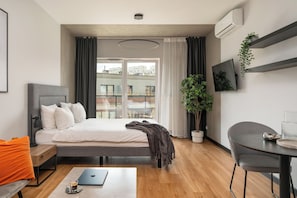 A modern hotel room with a bed, bedside table, laptop, and a view of the city through large windows. - apartamenty-wroc Center by Uni Bridge (Wrocław)