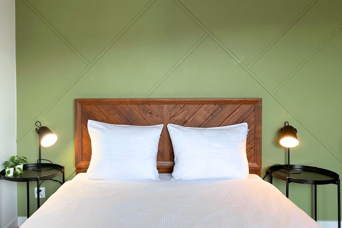 A bed with a wooden headboard, two bedside tables with lamps, and green walls.