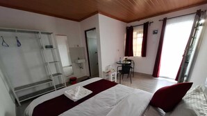 A hotel room with a large bed, a desk, a chair, a small table, a mirror, a wardrobe, and a window with curtains. - Jazby Guest House Naivasha (Naivasha)