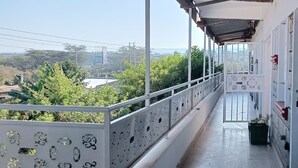 A covered balcony with a view of a green landscape, a tiled floor, and a railing with decorative elements. - Jazby Guest House Naivasha (Naivasha)