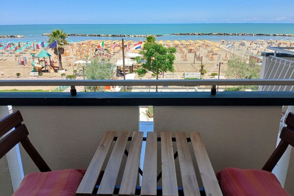 Un balcón con vista a la playa, que incluye una mesa y sillas de madera.