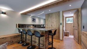 A modern kitchen with a central island, bar stools, and a wooden accent wall. - Val d'Isère - Flat for 7 ppl, 68 sqm (Val-d'Isère)