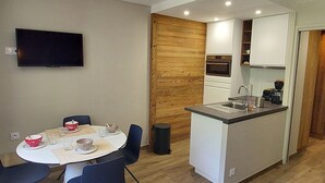 A compact kitchen with a dining area, a TV mounted on the wall, and a wooden accent wall.