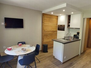 Uma cozinha compacta com área de refeições, uma TV fixada na parede e uma parede de destaque em madeira.