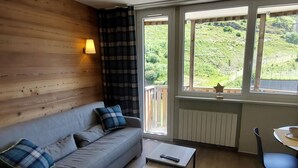 A room with a sofa, a small table, a chair, and a window with a view of greenery.