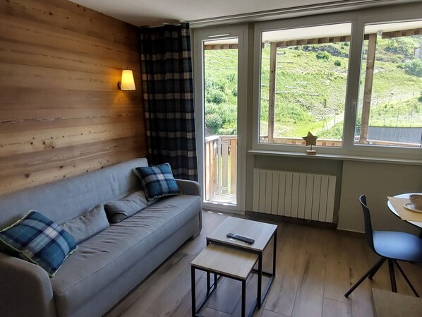 A room with a sofa, a small table, a chair, and a window with a view of greenery.