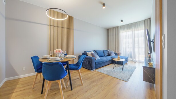 Una sala de estar moderna con un sofá azul, una mesa de comedor con sillas y un ventanal con cortinas.