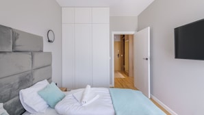 Un dormitorio con cama, armario, televisor y baño visible a través de una puerta abierta.