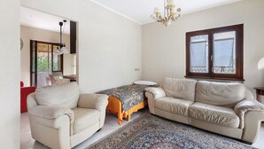 A room with a sofa, a small table, a chandelier, and a window with curtains.