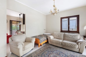 A room with a sofa, a small table, a chandelier, and a window with curtains.