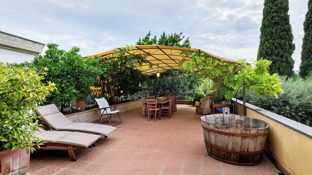 A patio with a wooden table, chairs, and lounge chairs under a pergola.