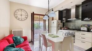 A modern kitchen with a dining area, a red sofa with green cushions, and a wall clock.