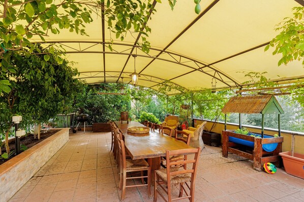 A covered patio with a long wooden table, chairs, and a play area with a slide and ball pit.