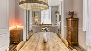 A dining area with a wooden table, chairs, a vase with dried flowers, a wicker chandelier, a lamp, a cabinet, and a view into another room. - Modernist Manor House for 14 – 7 Bedrooms – Central Palafrugell – Patio – Garage (Palafrugell)