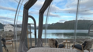 A room with a bed, two chairs, a table, and a view of a lake and mountains. - Arctic Glamping-Dome (Andoy)