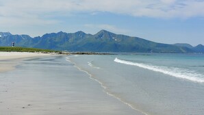 A beach with a lighthouse, calm waters, and mountains in the background. - Arctic Glamping-Dome (Andoy)