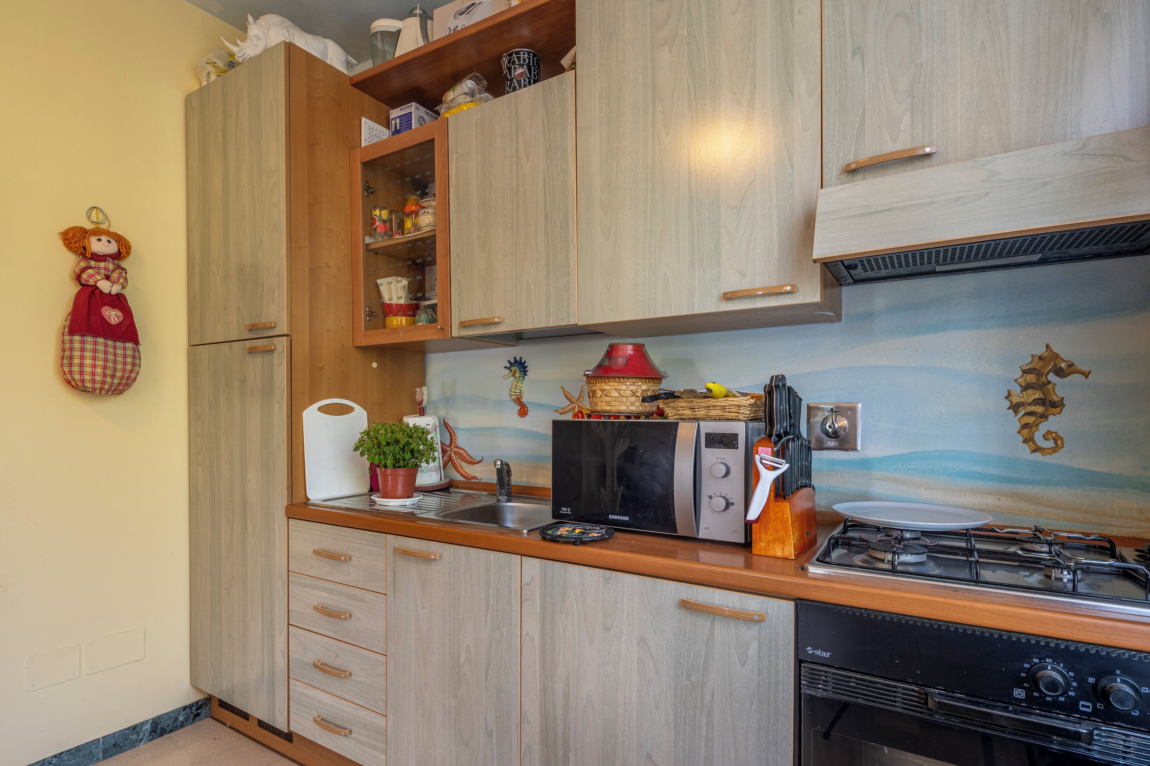 Una cocina con armarios de madera, un microondas, una estufa a gas y un caballito de mar decorativo en la pared.