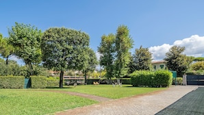 A paved pathway leading to a grassy area with trees and a building in the background. - Attico Marino (Marina di Pietrasanta)