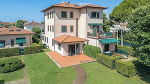 A multi-story building with a tiled roof, a small attached structure with a balcony, and a well-maintained lawn. - Attico Marino (Marina di Pietrasanta)