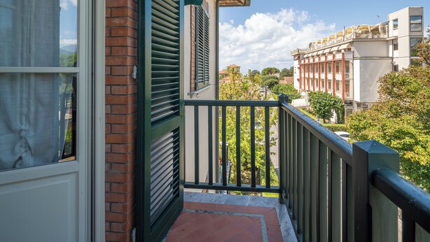 A balcony with a view of a cityscape, a brick wall, and a window with curtains. - Attico Marino (Marina di Pietrasanta)