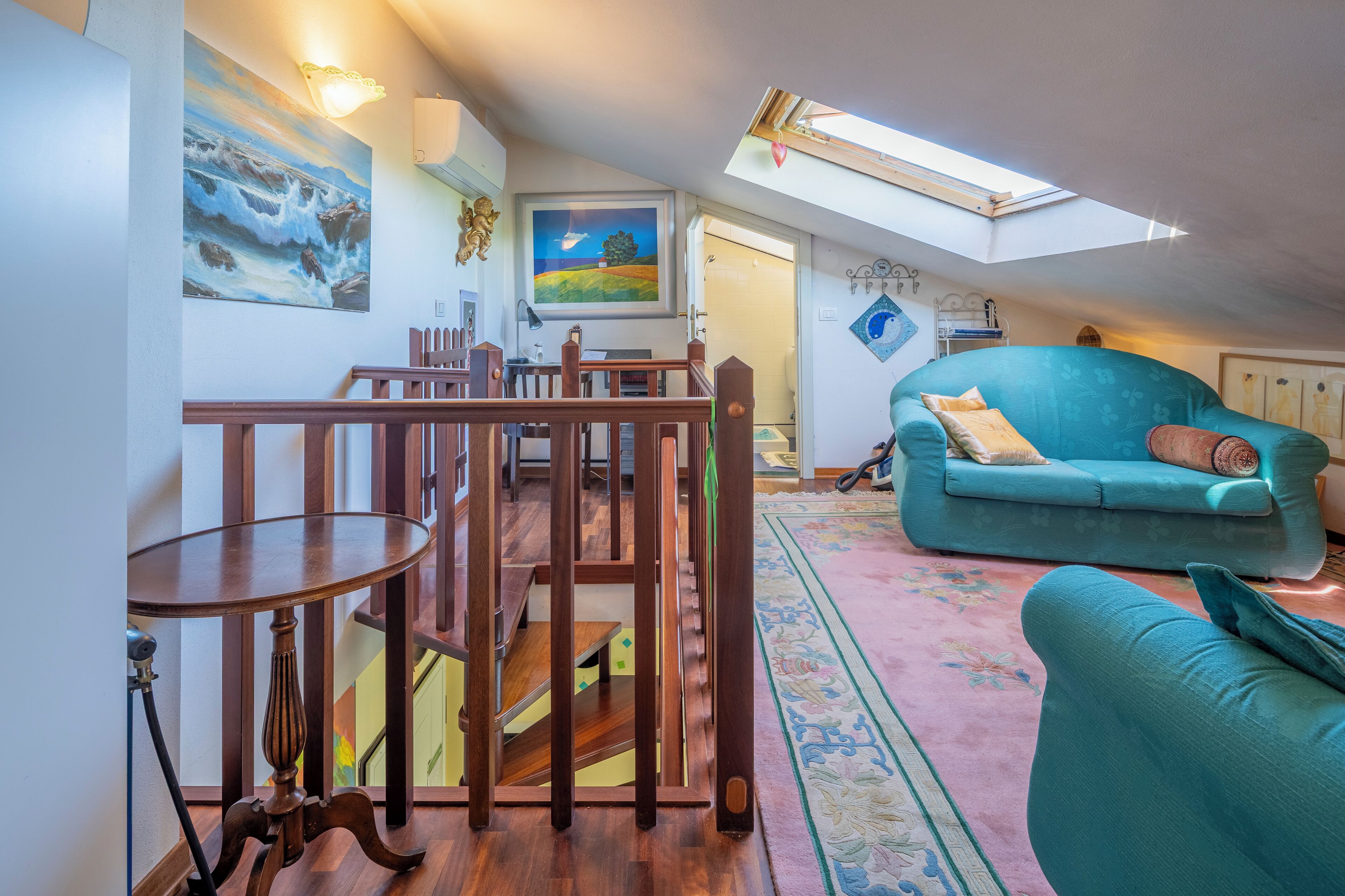 Un salon chaleureux avec un canapé de couleur turquoise, une table à manger en bois et une lucarne au plafond.