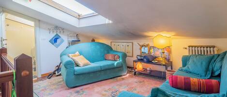 A cozy living room with a teal sofa, a pink floral rug, and a skylight above.