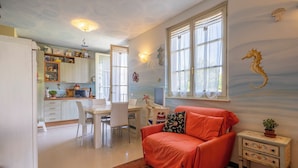 A compact living space with a dining area, kitchenette, and a cozy orange sofa. - Attico Marino (Marina di Pietrasanta)