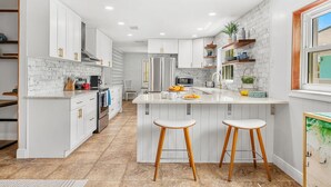 A modern kitchen with white cabinetry, a marble backsplash, and a central island with stools.