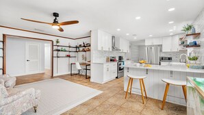 A modern kitchen with white cabinetry, a central island with stools, a ceiling fan, and a dining area with a chair and table.