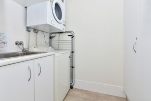 A laundry room with a washing machine, a sink, and a metal drying rack. - Ocean Shores Waterfront Escape in Nelson Bay (Nelson Bay)