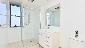 Ein modernes Badezimmer mit einer gläsernen Dusche, einem weißen Waschtisch mit Spiegel und einer Toilette.