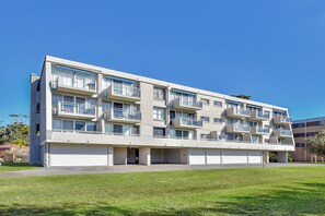 A multi-story residential building with balconies, a flat roof, and a parking area in front. - Ocean Shores Waterfront Escape in Nelson Bay (Nelson Bay)