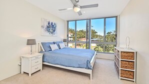 Ein Schlafzimmer mit einem Bett, einem Nachttisch, einer Lampe und einem großen Fenster mit Blick.