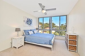 A bedroom with a bed, nightstand, lamp, and a large window with a view.